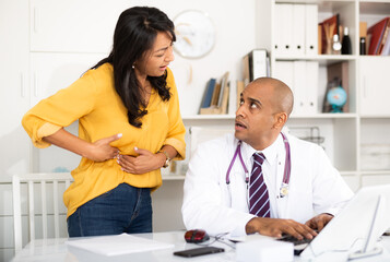Obraz premium Focused physician attentively listening to female patient suffering from stomachache in medical office.