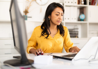 Latin American businesswoman sitting in office at workplace and working at laptop