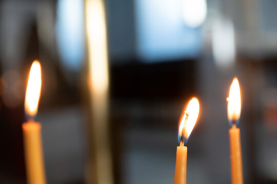 Festive and religious concept: There are three candles but the focus is on a single yellow candle in the middle with hot flame. Blurry background