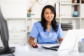 Nurse working on PC in modern private clinic with white walls