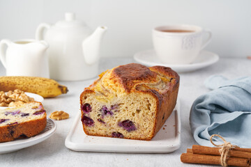 Banana bread, sliced cake with banana and blueberries. Morning breakfast with tea on light gray cincrete background