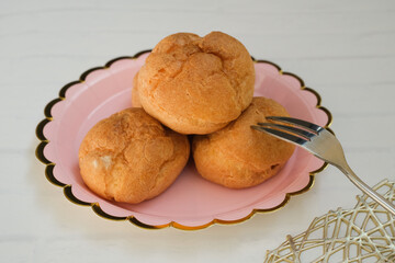 Homemade choux cream or Choux Pastry or Profiterole or Eclair or cream puff on pink plate near the dessert fork on white wooden background. French dessert concept. selected focus.