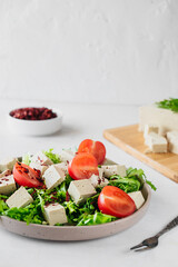 healthy vegan diet salad of tofu, herbs and tomatoes on white table. two-pronged fork, block of cheese on cutting bamboo board, and bowl of spices on background. Dinner idea at home, selective focus