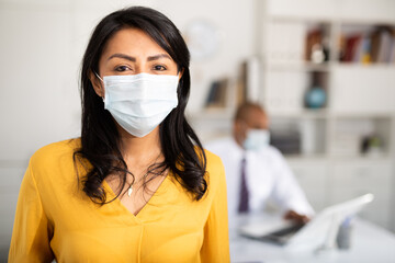 Secretary of the chief physician in protective mask is standing with documents in clinic