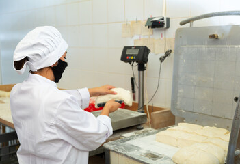 Professional hispanic female baker portioning dough with scraper and weighing pieces