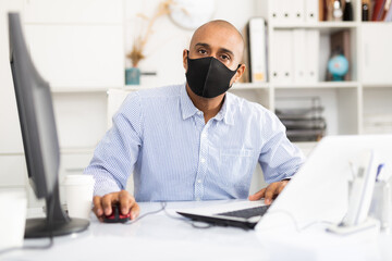 Office worker in a protective mask works behind a laptop