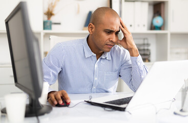 Fototapeta premium Portrait of handsome hispanic employee looking at camera and sitting at office desk
