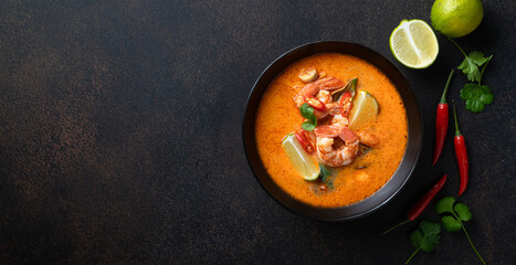 Tom Yam kung Spicy Thai soup with shrimp in a black bowl on a dark stone background, top view, copy...