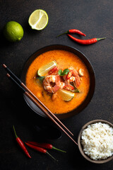 Tom Yam kung Spicy Thai soup with shrimp in a black bowl on a dark background, top view