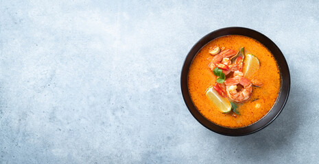 Tom Yam kung Spicy Thai soup with shrimp in a black bowl on a blue concrete background, top view,...