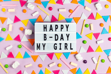 Fototapeta na wymiar White board with the inscription happy birthday my girl on a pink background with a multi-colored garland of felt, candles, candies and marshmallows greeting card
