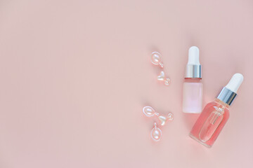 bottles of cosmetic serum and skin care oil and single-dose capsules on pink background. face care...