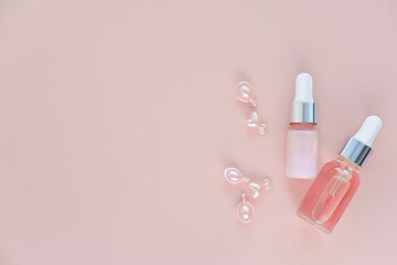 bottles of cosmetic serum and skin care oil and single-dose capsules on pink background. face care and beauty concept. anti age treatment. collagen serum and capsules.