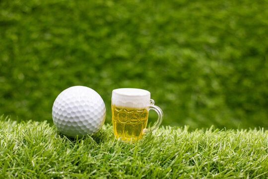 Golf ball and glass of beer on green grass background