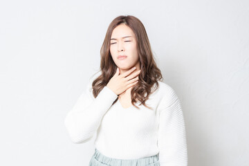 白い壁の前に立つ、喉が痛いジェスチャーをする若い女性