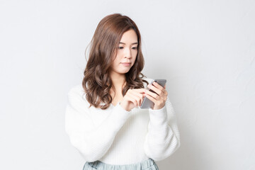 白い壁の前に立って、スマホを使う若い女性