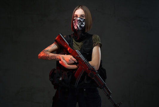 Dressed in dark armour and shirt female soldier with short haircut and weared with mask poses holding ak74 rifle.