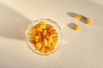 Raisins of yellow grapes in a glass plate on a beige background in bright sunlight. Healthy sweets. Winter vitamins.