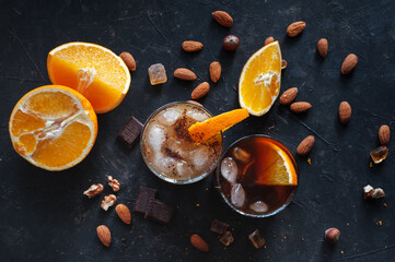 Cold espresso coffee with ice and orange juice in two glass glasses on a dark table with nuts, chocolate and orange. A brisk summer drink. View from above.