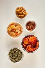 Different dried fruits and nuts in white plates on a light background. A healthy snack. Winter vitamins. View from above. Vertical photo.