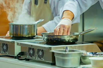 Hands of a cook who is cooking something. He is frying a dish in a frying pan. Cook is adjusting something in pan. Concept is a master class from the chef. Master class on playing a dish.