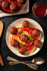 Meatballs with tomato sauce and pasta, with a glass of wine, shot from the top on a black background