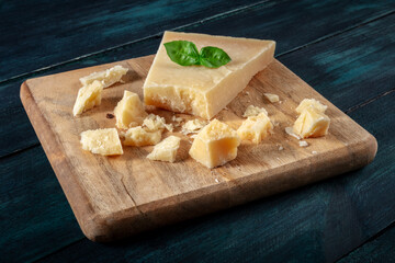 Crumbled Parmesan cheese with basil leaves, on a wooden cutting board on a dark blue wooden background