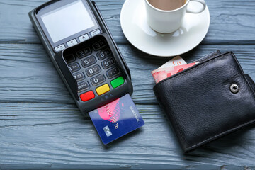 Payment terminal with credit card, wallet and cup of coffee on table