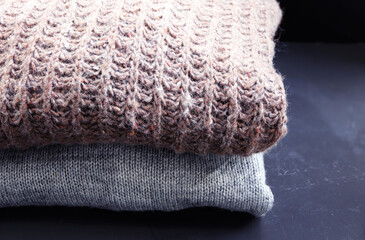 Stack of cozy knitted sweaters on black wooden background. Autumn-winter concept