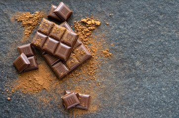 Broken pieces of chocolate and cocoa powder on a wooden background