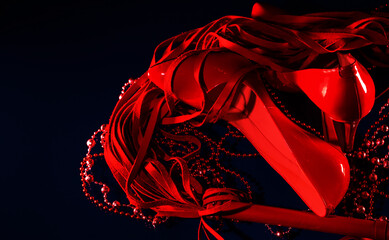 patent leather shiny female red stilettos, whip and beads on a black background