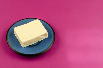 Rectangular piece of processed cheese in a blue saucer on a pink background.