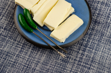 Rectangular slice of processed cheese in a blue saucer on a denim background.
