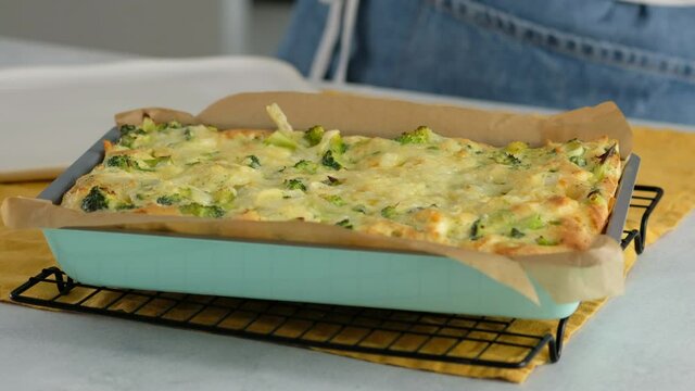 Close-up. Female hand putting hot form with a frittata on the grid. Italian breakfast. Baked chopped omelet with vegetables and broccoli on a serving plate. Healthy breakfast.