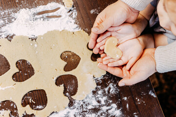 Cookies in shape of heart for the Saint Valentine's Day. Father and daughter are making heart shape cookies. Dough, flour and baking pan on the table.