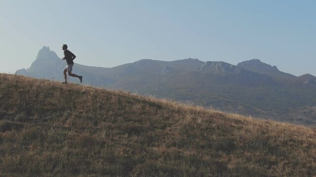 Man is running up to hilltop from right to left. Scene is showing a mountain peak background and hill edge in that appears the running man