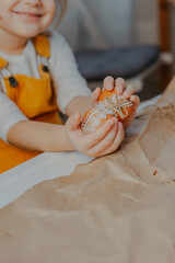 Baby girl decorating easter eggs on white table. Kid decorating eggs with kraft paper, lace and rope. Child holds easter eggs in hands.