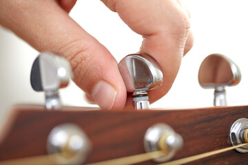 music and musical instruments concept - close up of hand tuning guitar strings with pegs