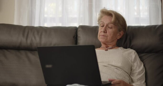 Older women have to work from home with online training meetings and she was in a comfortable position leaning on the sofa at her home alone.