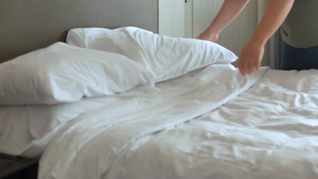 Housekeeper is making the bed in the room- place pillow into the bed