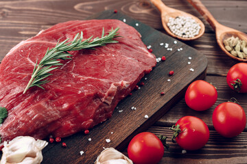 Raw beef steak with rosemary and spices on wooden board