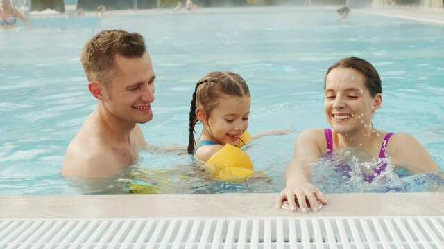 Slow-motion chest-up shot of cheerful young caucasian family having fun together in roofed thermal swimming pool