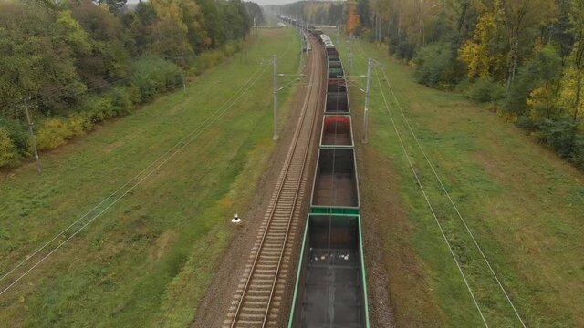 Top view of the empty gondola cars of a freight train passing through a picturesque wooded countryside in autumn. Concept of railway transport