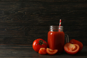 Jar with tomato juice and straw and tomatoes on wooden background