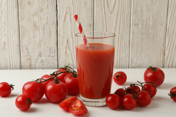 Glass with tomato juice and straw and tomatoes on wooden background
