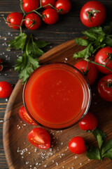 Glass of tomato juice, tomatoes and salt on wooden background