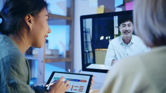 Asia businesswomen using desktop talk to colleagues about plan in video call meeting at living room. Working from house overload at night, remotely work, social distancing, quarantine for coronavirus.
