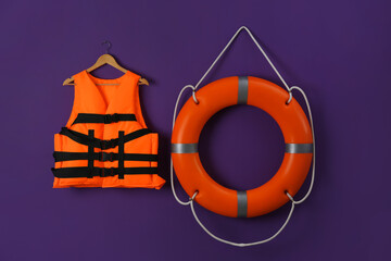 Orange life jacket and lifebuoy on violet background. Rescue equipment