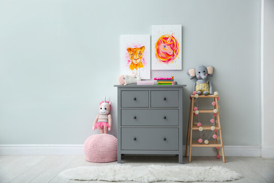 Cute pictures and chest of drawers with toys in baby room interior. Space for text