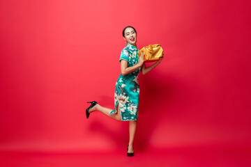 Happy smiling Asian woman in traditional costume holding gold gift box in red isolated studio background for Lunar new year concepts